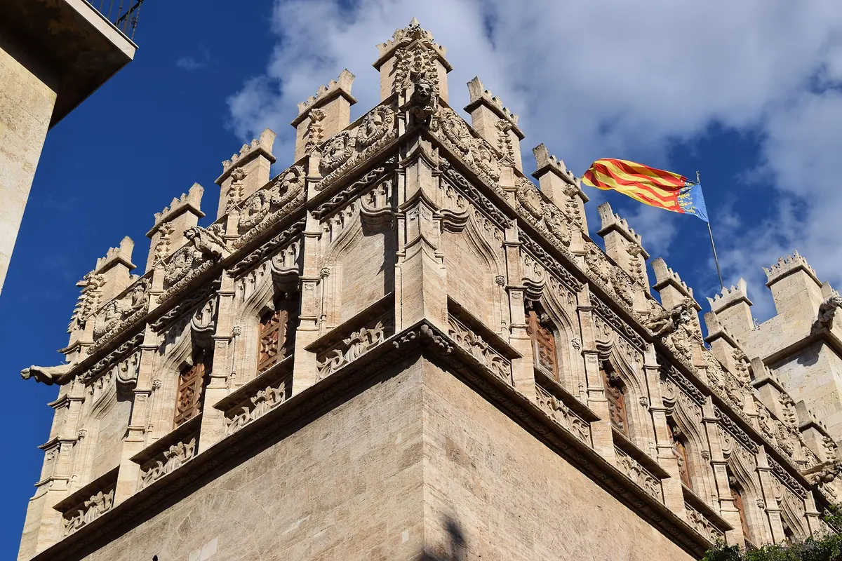 Det krenelerede stenhjørne af Silbørsen i Valencia med udskårne vinduer og et flag mod en blå himmel